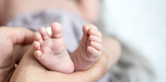 Contato com hormônio dos pais pode causar alterações em bebê Close up of a mom holding the little feet of a newborn baby.